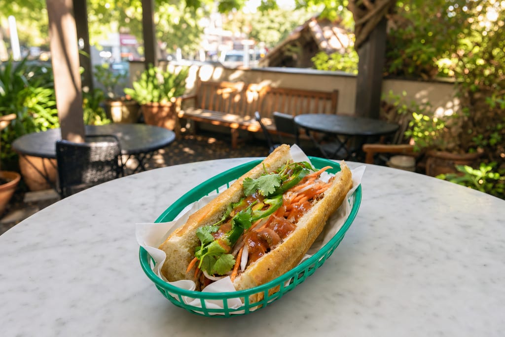 BBQ pork banh mi: glazed pork slices, pickled carrot and daikon, jalapeño and cilantro in a green basket on the patio