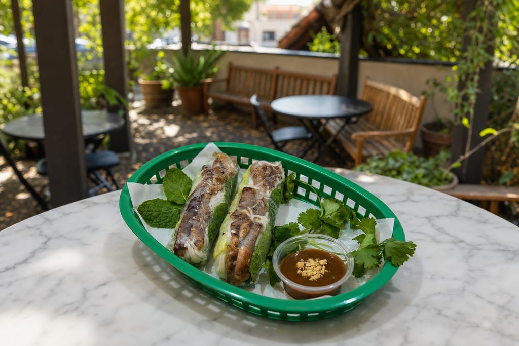 Pork spring rolls: two whole rolls of grilled pork, lettuce and vermicelli, with peanut sauce and herbs in a green basket