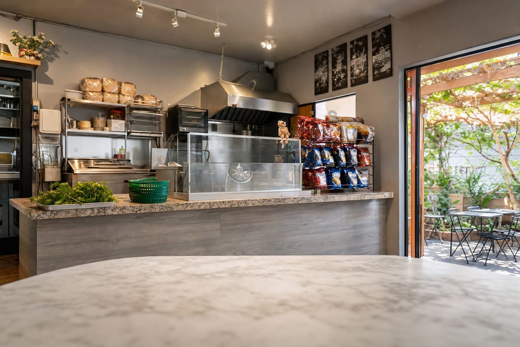The order counter with a speckled stone top, glass display case and stacked green baskets, an open door to the patio beyond